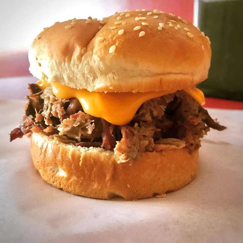 Close-up of a Lakeside Barbeque & Subs pulled pork sandwich with melted cheese on a sesame seed bun.