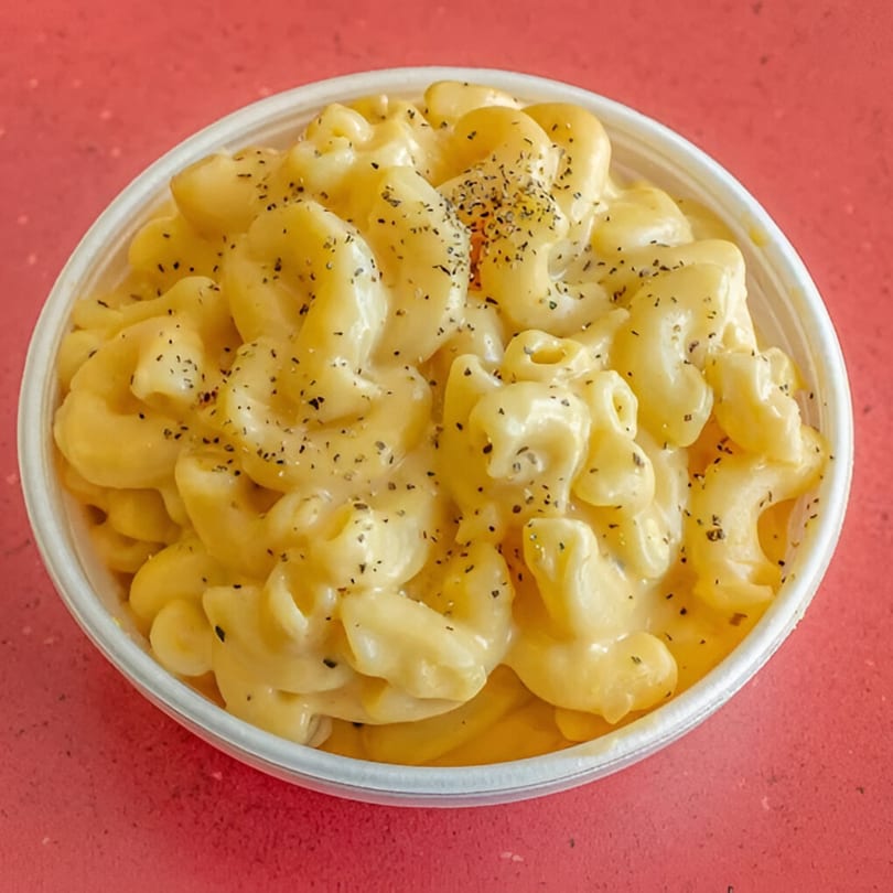 A white bowl filled with creamy macaroni and cheese, topped with black pepper, on a red background.